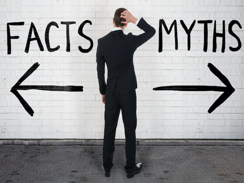 Rear view of confused businessman looking at arrow signs below facts and myths text contemplating his hearing loss.