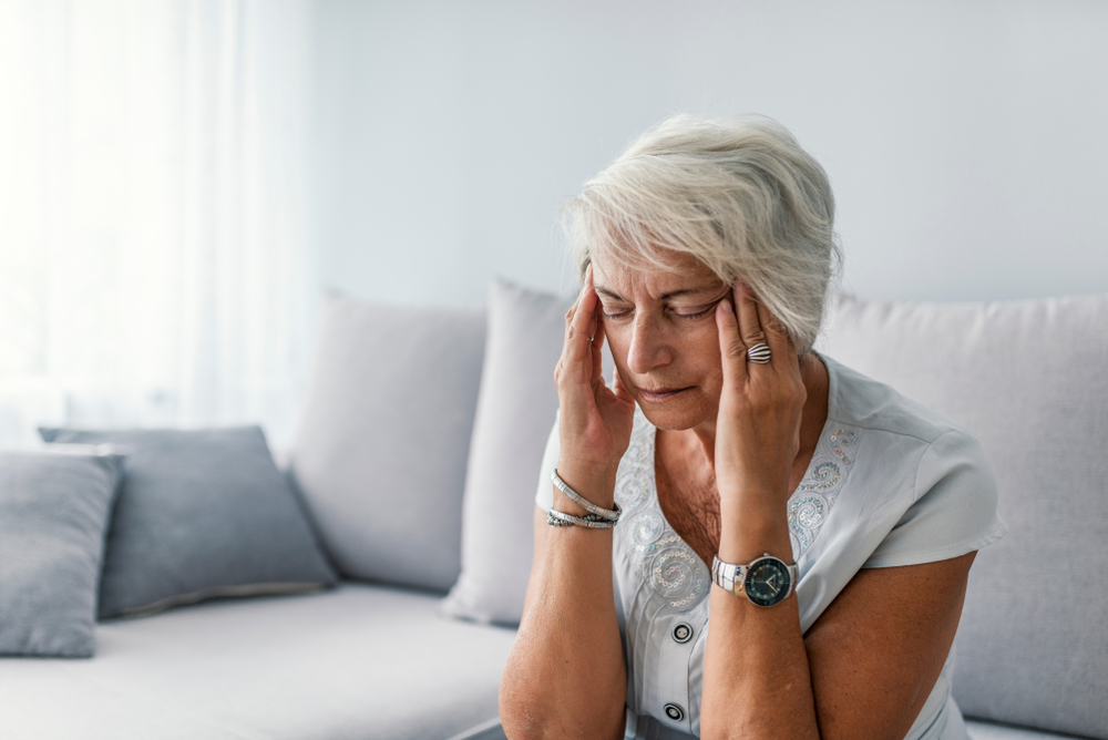 A mature woman suffering from a headache at home on the sofa.