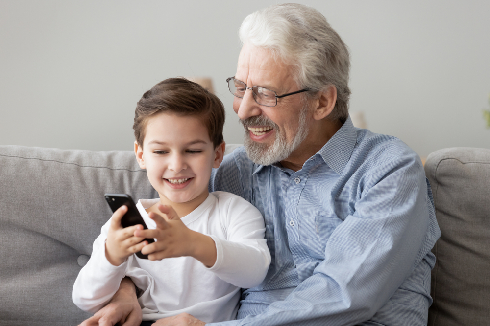 Grandfather and small grandson using smart phone apps at home.