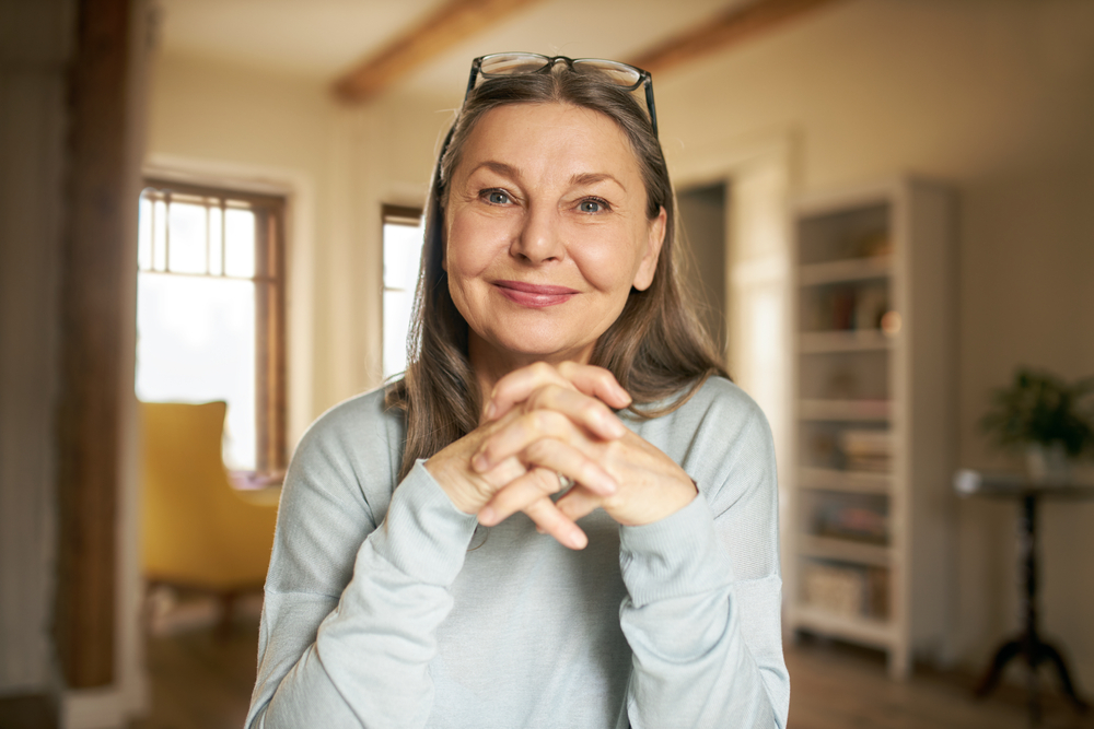 Woman in grey shirt looking at the camera with a happy smile.