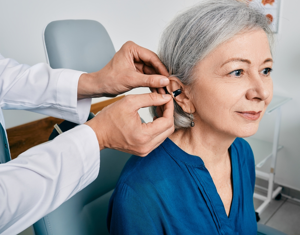 woman during installation hearing aid into her ear by her audiologist.