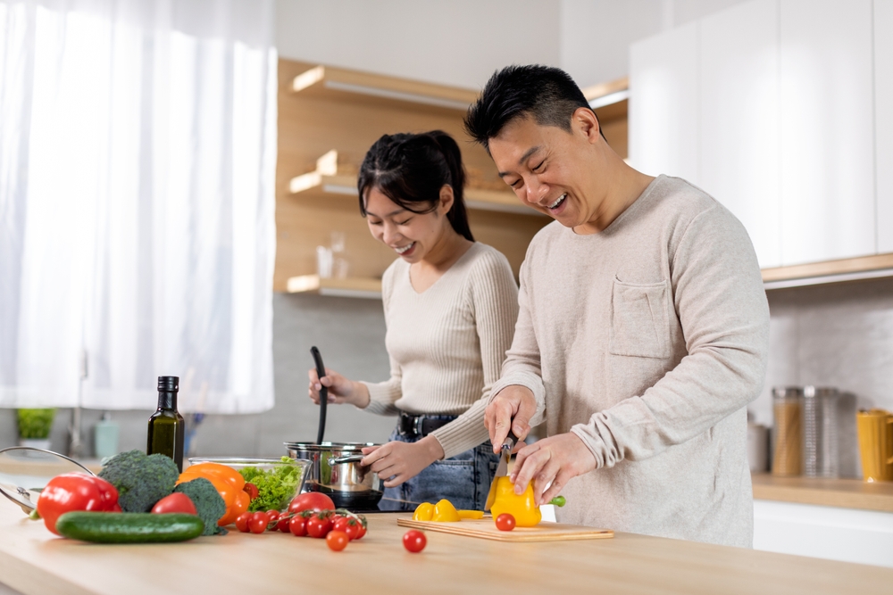 Man and woman cooking and chopping vegetables in kitchen.