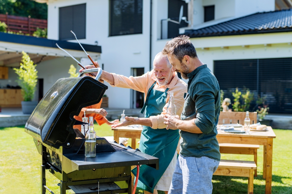 Senior father with adult son grilling outside in backyard.