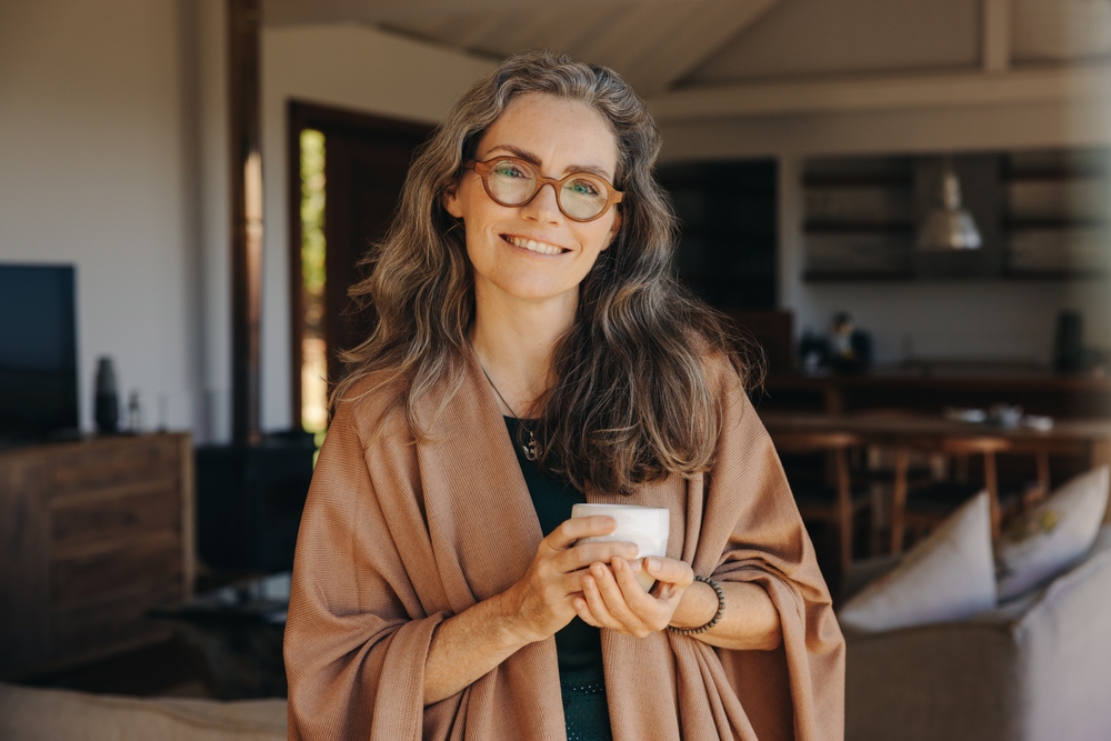 woman smiling at the camera while standing with a cup of tea in her hands.