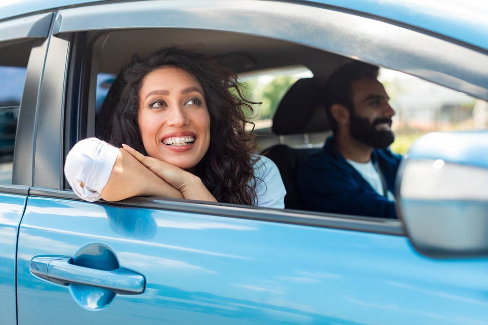 Woman and man driving with windows down in car.