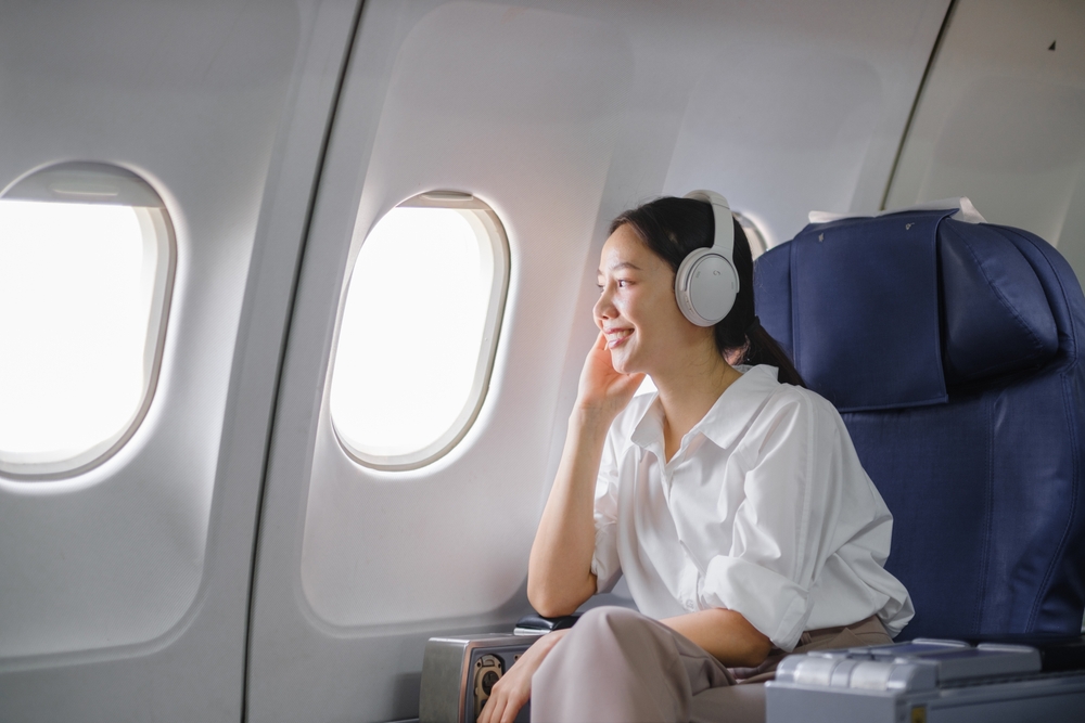 Woman sitting in airplane seat with headphones on.