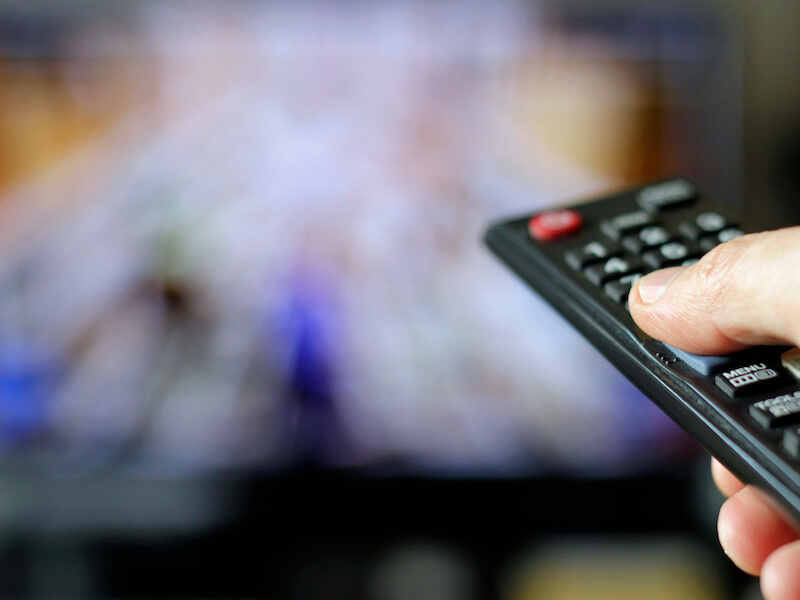 Up close look at a thumb pressing the up button on the volume function of a tv remote.