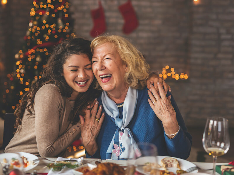 Family having Christmas dinner at home, gathered around the table, enjoying their time together; daughter hugging her mother and smiling