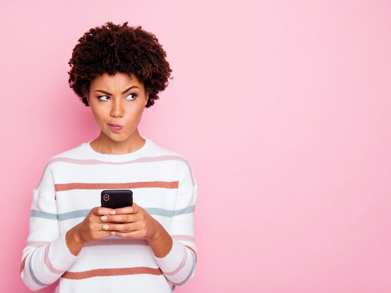 Woman with short curly hair reading about hearing tests on her phone contemplating scheduling and exam