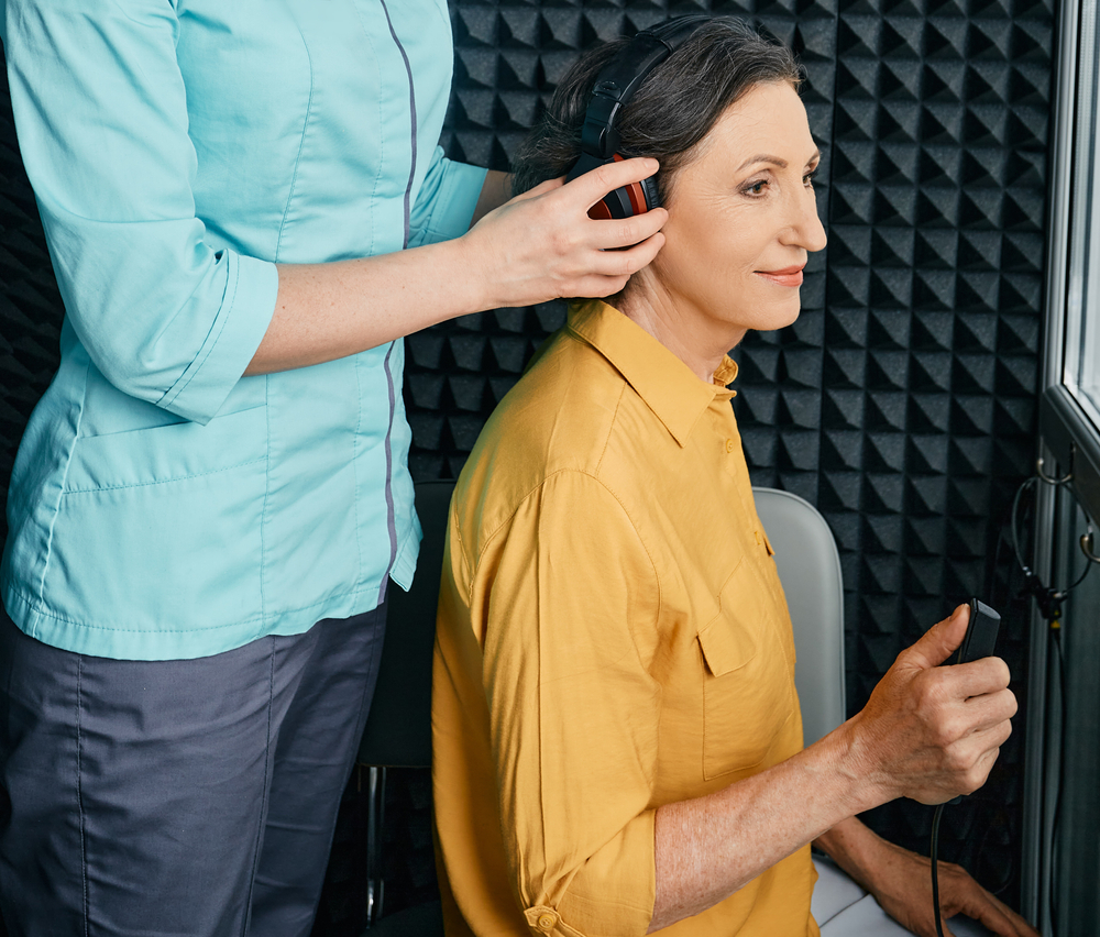 hearing specialist places headphones on patient for hearing test.